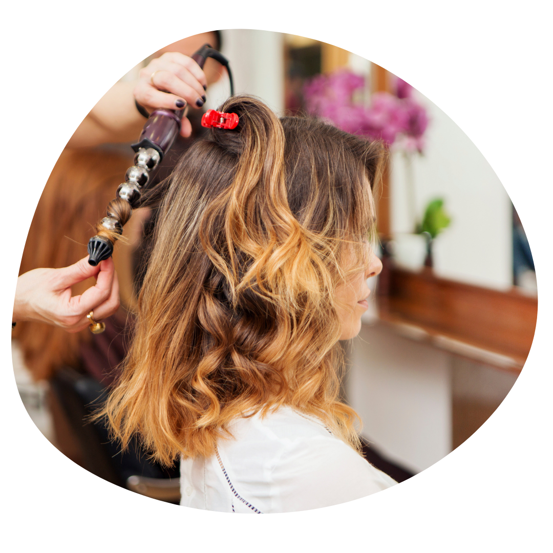 Stylist curling a woman's hair with a curling iron in a salon.